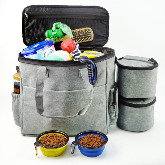 Gray pet travel bag with pet supplies including bowls, food, and a brush on a white background