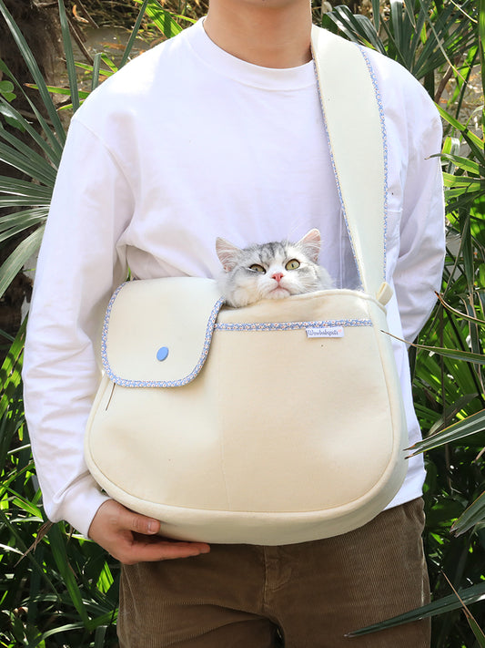Person holding a beige pet carrier with a cat peeking out, surrounded by green foliage.