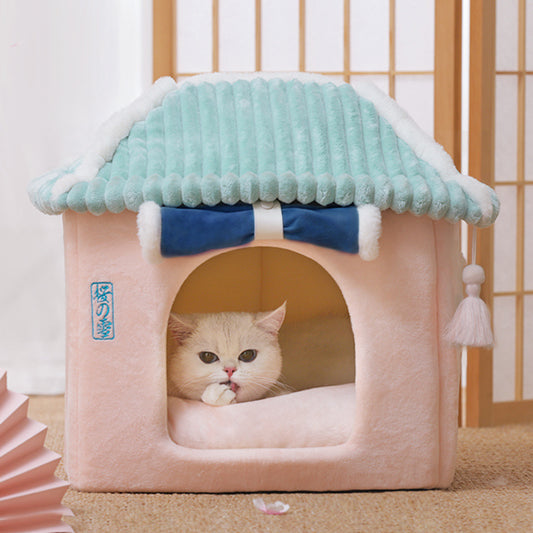 Cat peeking out from a pink pet house with a blue roof and white tassels.
