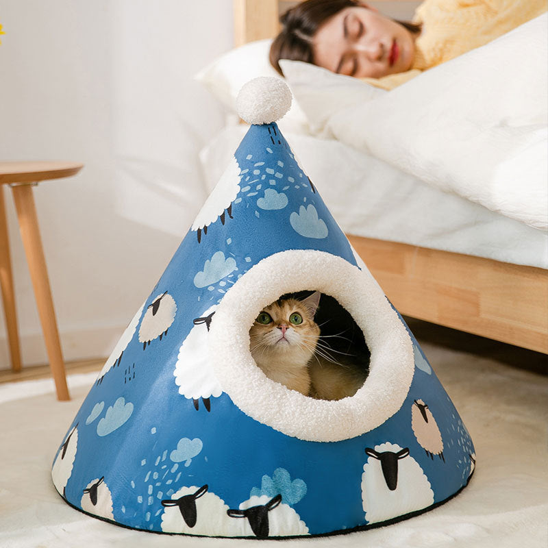 Cat inside a blue cone-shaped pet bed with sheep pattern, person lying on bed in background