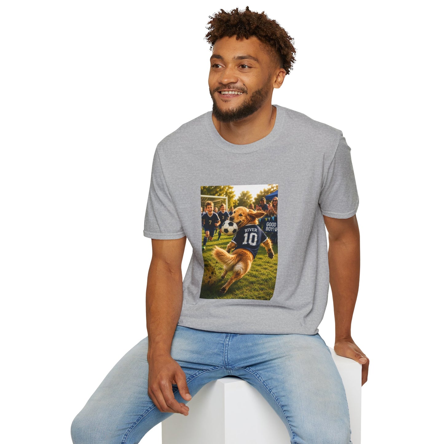  man wearing a gray  graphic t-shirt and light blue jeans, sitting on a white block against a plain white background. The t-shirt features a rectangular graphic print showing a golden retriever dog playing football with players wearing navy jerseys.