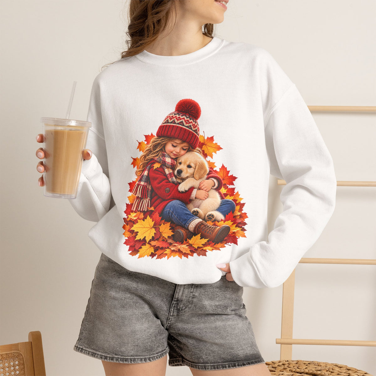 Woman holding a drink while wearing the white Golden Moments girl and puppy fall sweatshirt