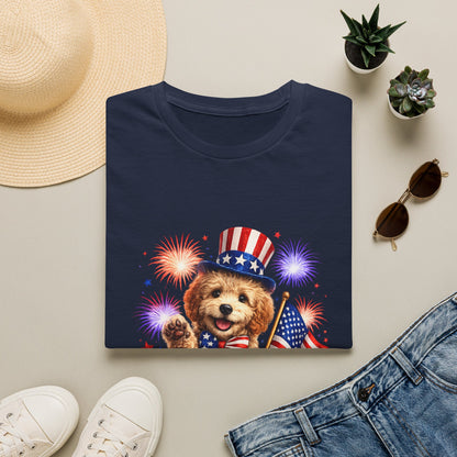 Navy blue t-shirt with a dog wearing an American flag hat and holding a flag, surrounded by fireworks on a beige surface with a hat, sunglasses, and jeans.
