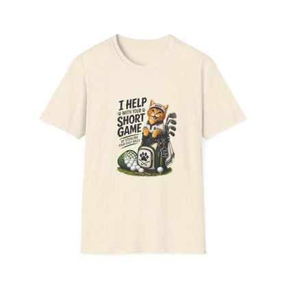 A natural color graphic T-shirt is displayed in a styled flat lay on a light beige surface. The shirt features a cartoon cat wearing a baseball cap and holding golf clubs, with the text 'I HELP WITH YOUR SHORT GAME BY STEALING GOLF BALLS.