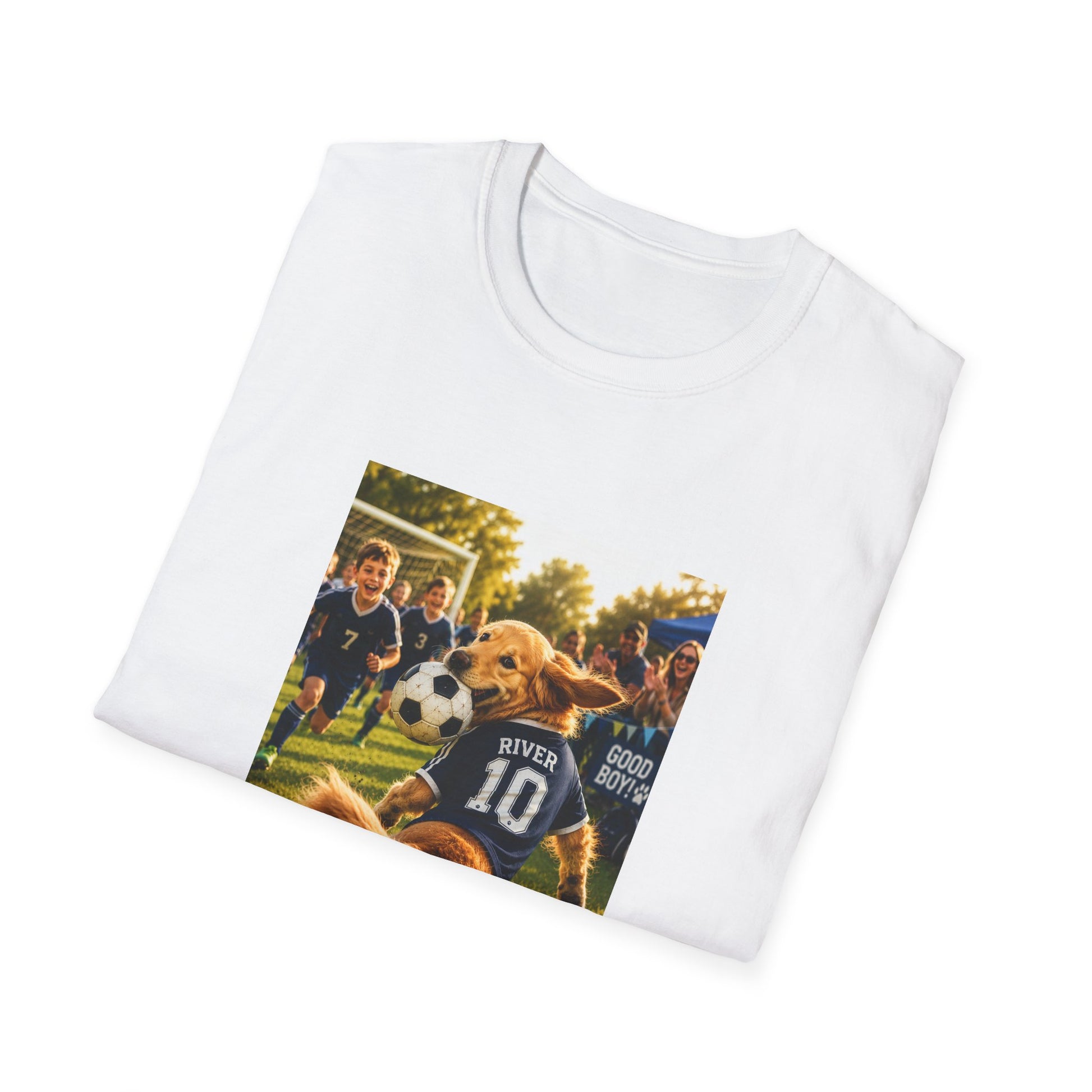 A white folded crewneck t-shirt with a custom printed graphic on the front. The graphic shows a golden retriever dog wearing a soccer jersey with the name 'RIVER' and number '10' on the back, playing with a soccer ball on a grassy field with children in the background.