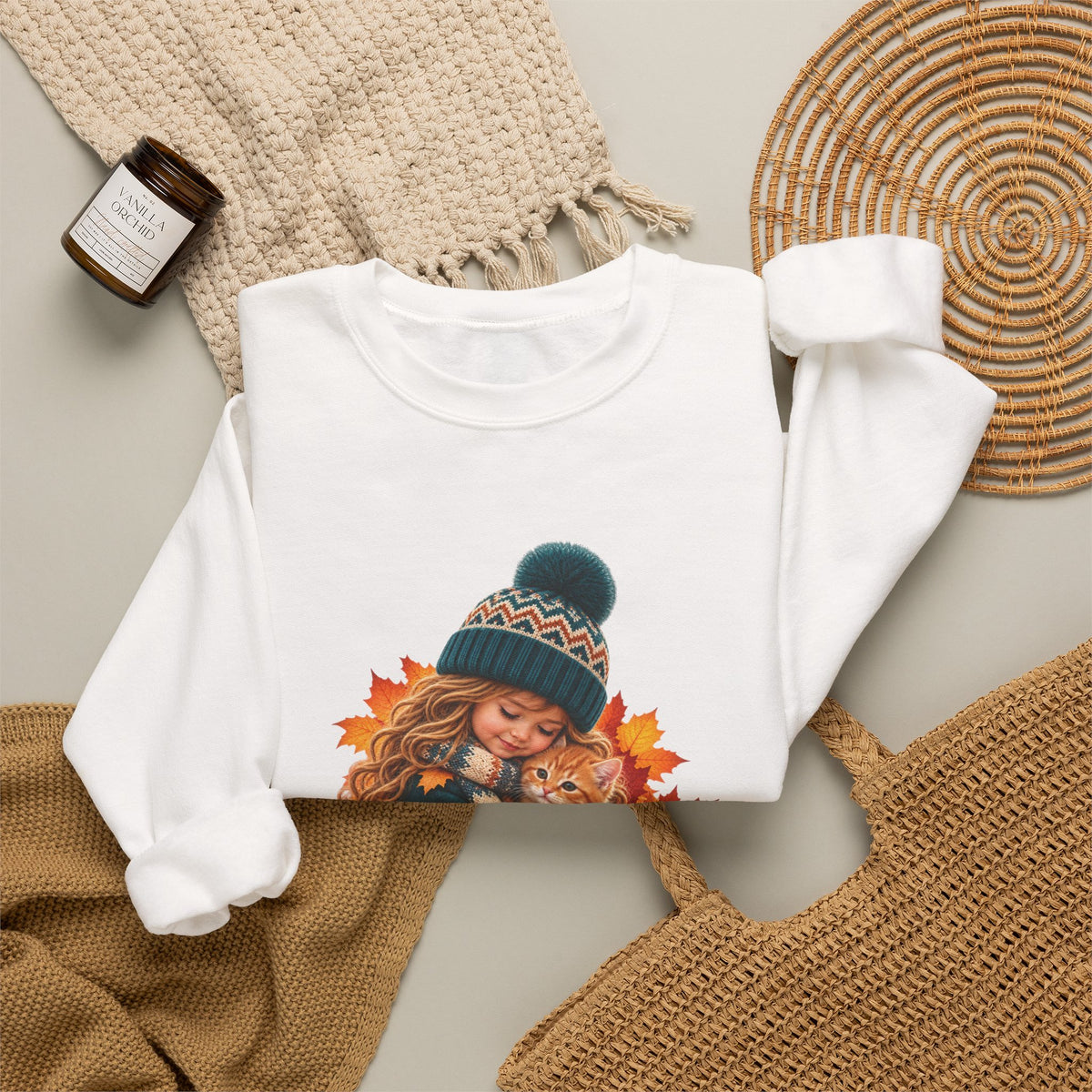 Folded white Golden Moments girl and kitten sweatshirt styled with neutral knit accessories
