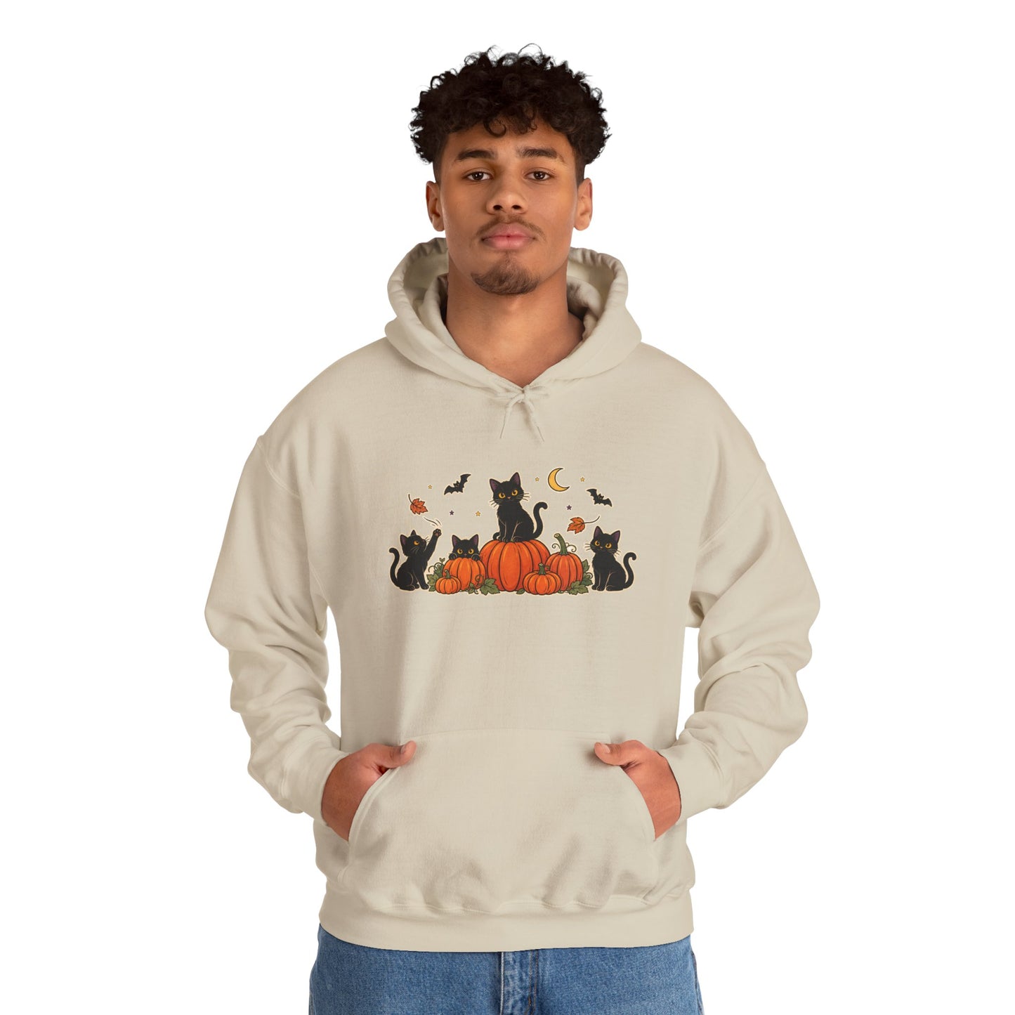 A man wearing a light beige hoodie with a graphic print of black cats sitting on orange pumpkins with bats, a crescent moon, and acorns. He is standing against a plain white background.