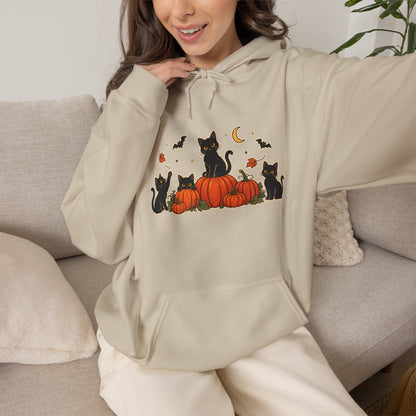 A woman wearing a beige hoodie with a graphic of black cats around orange pumpkins and small bats, sitting on a light gray couch.