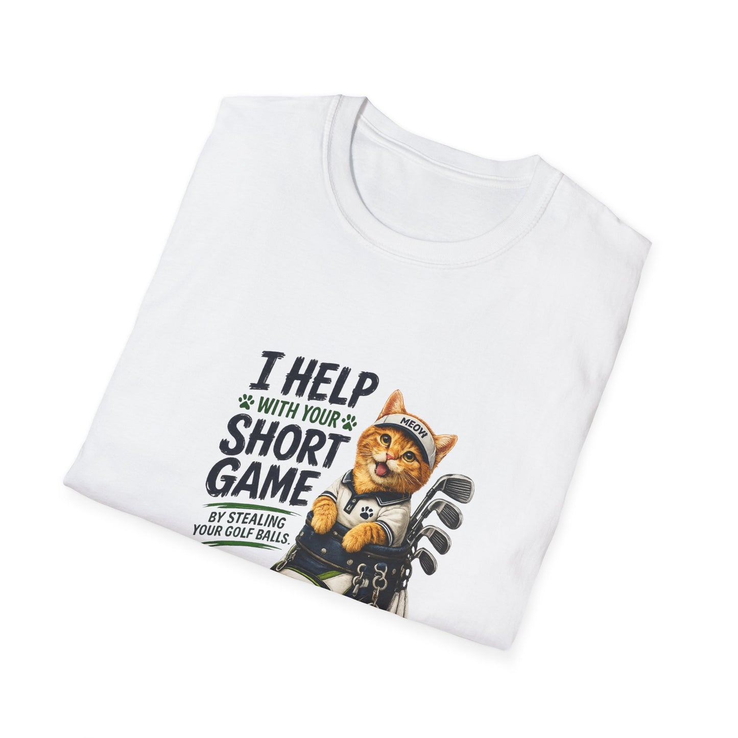 A folded white graphic T-shirt is displayed in a styled flat lay on a light beige surface. The shirt features a cartoon cat wearing a baseball cap and holding golf clubs, with the text 'I HELP WITH YOUR SHORT GAME BY STEALING GOLF BALLS.