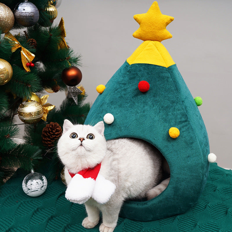 Cat in a Christmas tree-shaped pet bed with a decorated Christmas tree in the background