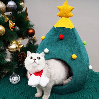 Cat in a Christmas tree-shaped pet bed with a decorated Christmas tree in the background