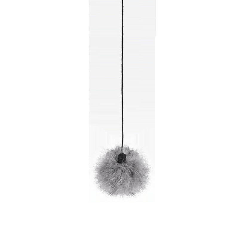 Gray fur pom-pom hanging from a black string on a white background