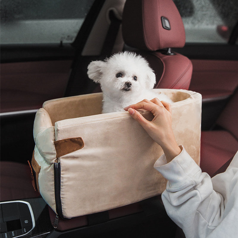 Small white dog in a beige pet car seat inside a vehicle.