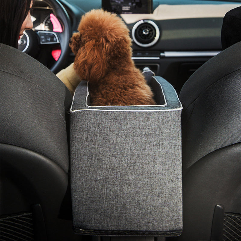 Dog sitting in a car with a gray pet barrier between the front seat and driver.