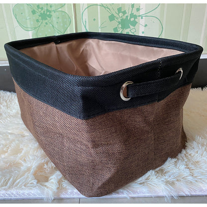 Brown and black fabric basket on a white surface with a floral-patterned curtain in the background.