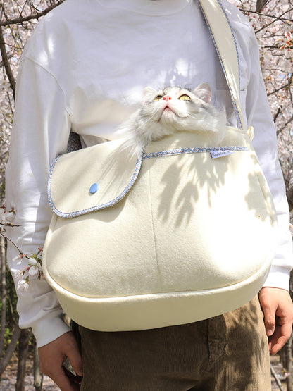 Person carrying a cream-colored backpack with a fluffy white cat peeking out, set against a natural background.