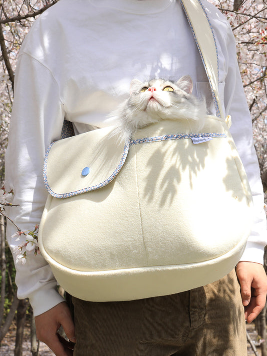 Person carrying a cream-colored backpack with a fluffy white cat peeking out, set against a natural background.