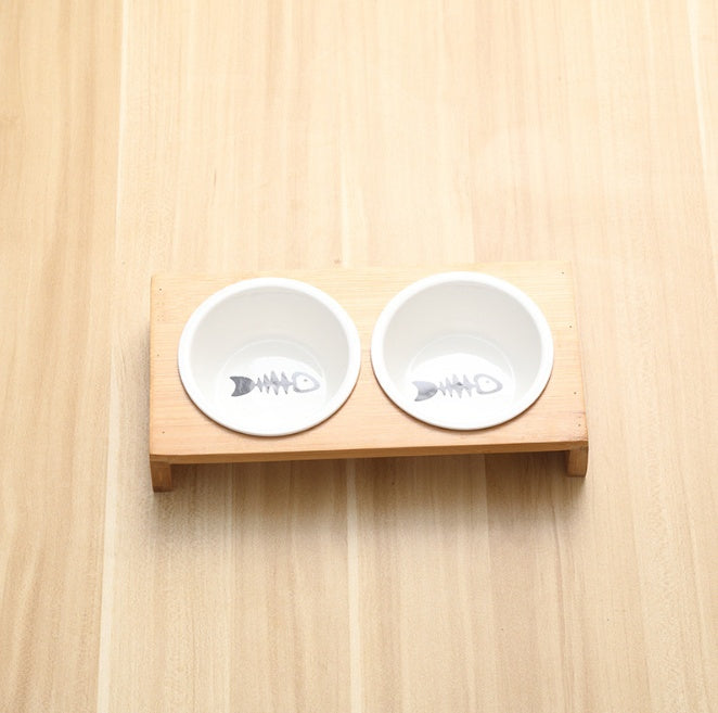 Two white pet bowls with fish bone design on a wooden surface