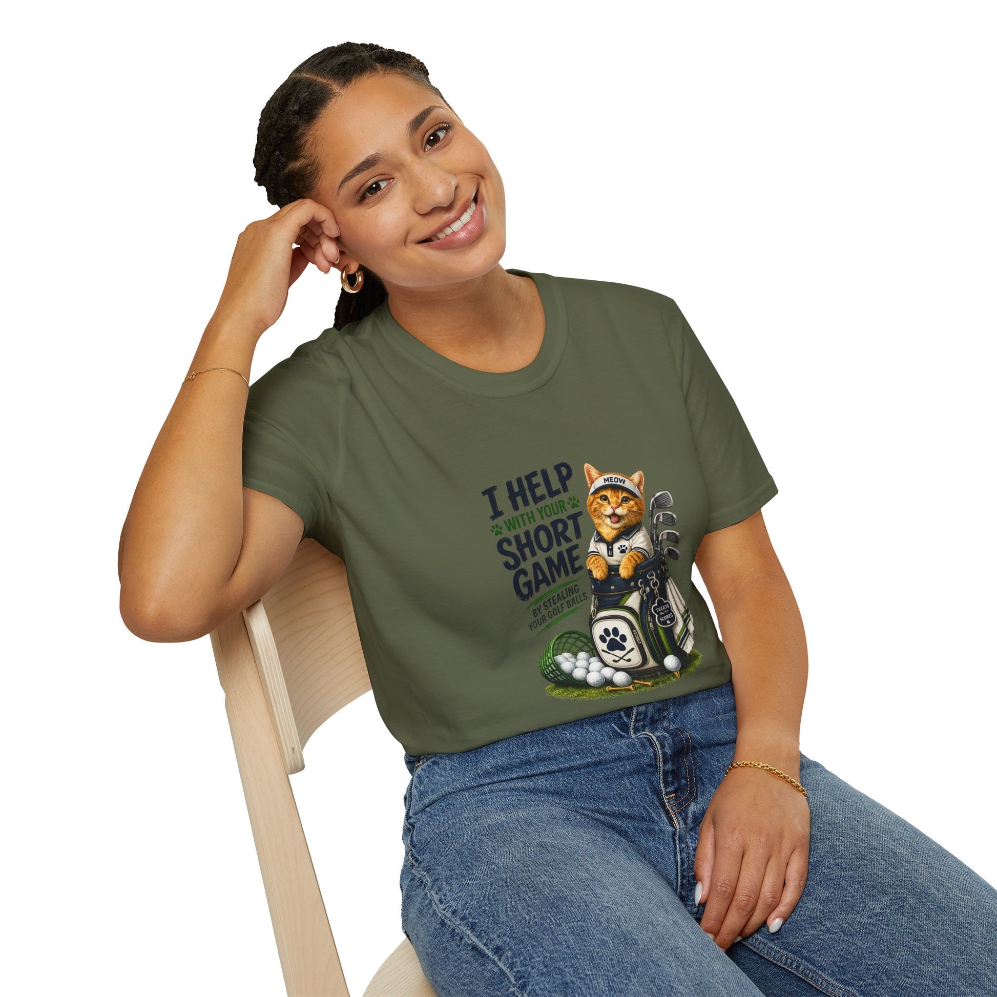 A military green graphic T-shirt is displayed in a styled flat lay on a light beige surface. The shirt features a cartoon cat wearing a baseball cap and holding golf clubs, with the text 'I HELP WITH YOUR SHORT GAME BY STEALING GOLF BALLS.