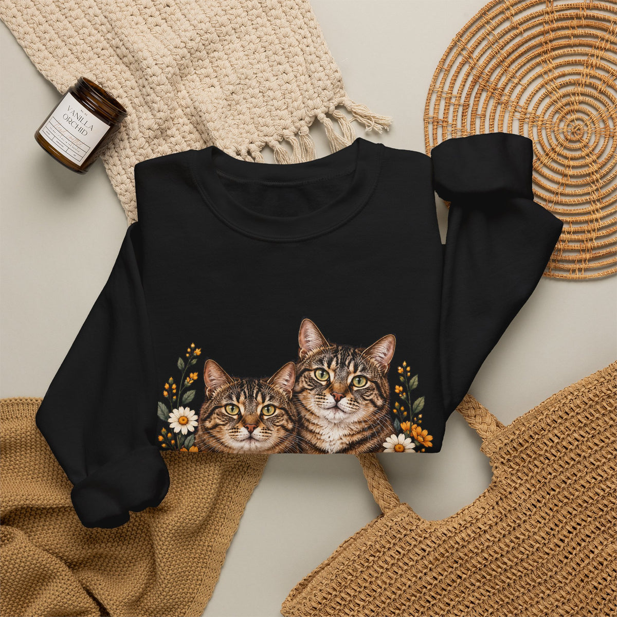 Folded black crewneck sweatshirt featuring two tabby cats surrounded by orange and white wildflowers