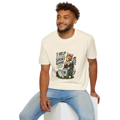 A natural color graphic T-shirt is displayed in a styled flat lay on a light beige surface. The shirt features a cartoon cat wearing a baseball cap and holding golf clubs, with the text 'I HELP WITH YOUR SHORT GAME BY STEALING GOLF BALLS.