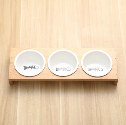 Three white ceramic bowls with fish bone designs on a wooden holder against a light wood background