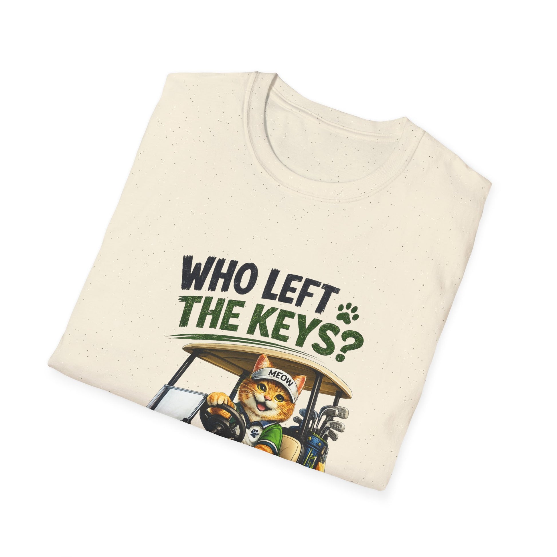 A folded cream-colored t-shirt with a graphic print of a cartoon cat driving a golf cart, with the text 'WHO LEFT THE KEYS?' in dark green and black lettering.