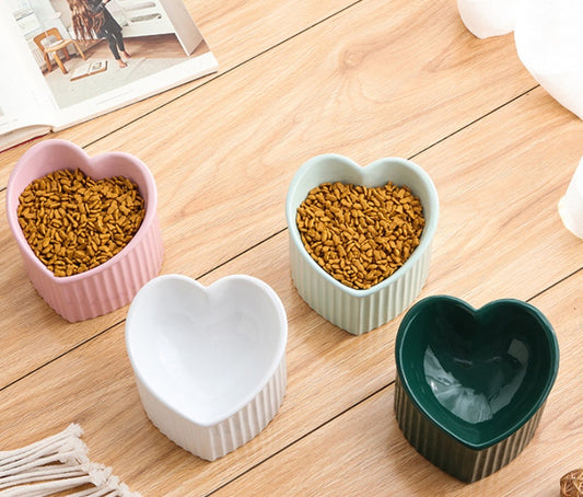 Heart-shaped ceramic bowls filled with pet food on a wooden floor.