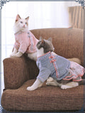 Two cats wearing matching outfits sitting on a brown couch.