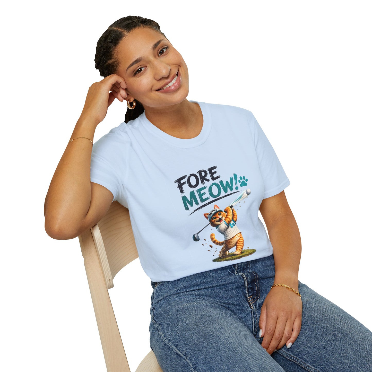A woman wearing a light blue graphic t-shirt with a cartoon cat playing golf and the text 'FORE MEOW!'. She is sitting on a wooden chair against a white background.