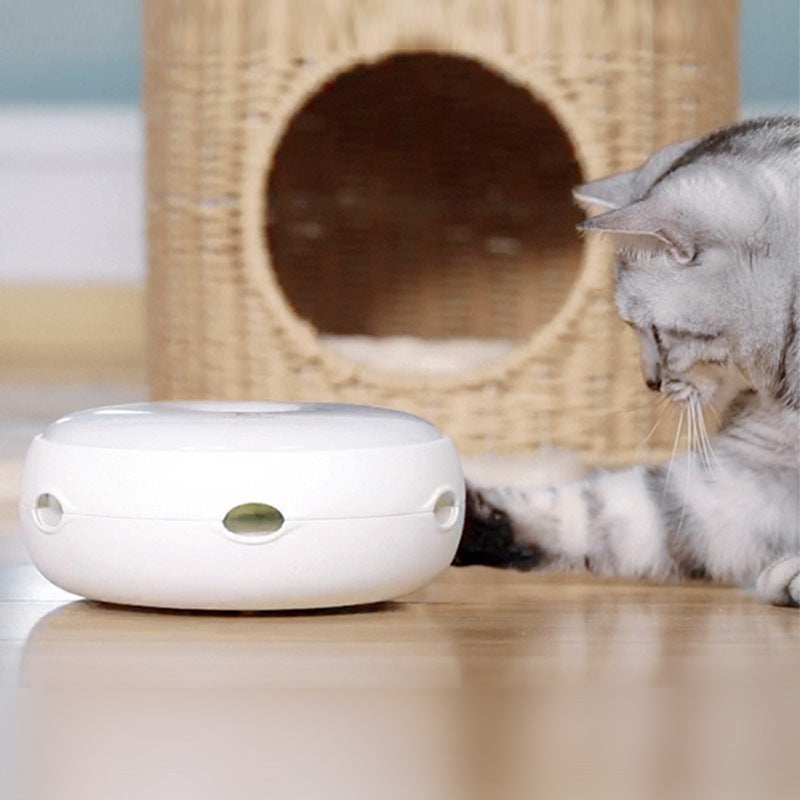 Cat interacting with a white electronic device on a wooden floor with a wicker cat bed in the background.