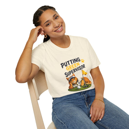A woman sitting on a wooden chair wearing a cream-colored graphic t-shirt with a cartoon tiger and the text 'PUTTING GREEN SUPERVISOR' in navy and yellow, paired with blue jeans, against a solid white background.