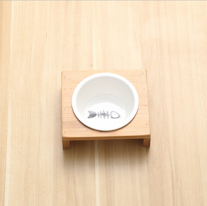 White ceramic bowl with fish skeleton design on a wooden stand against a light wood background