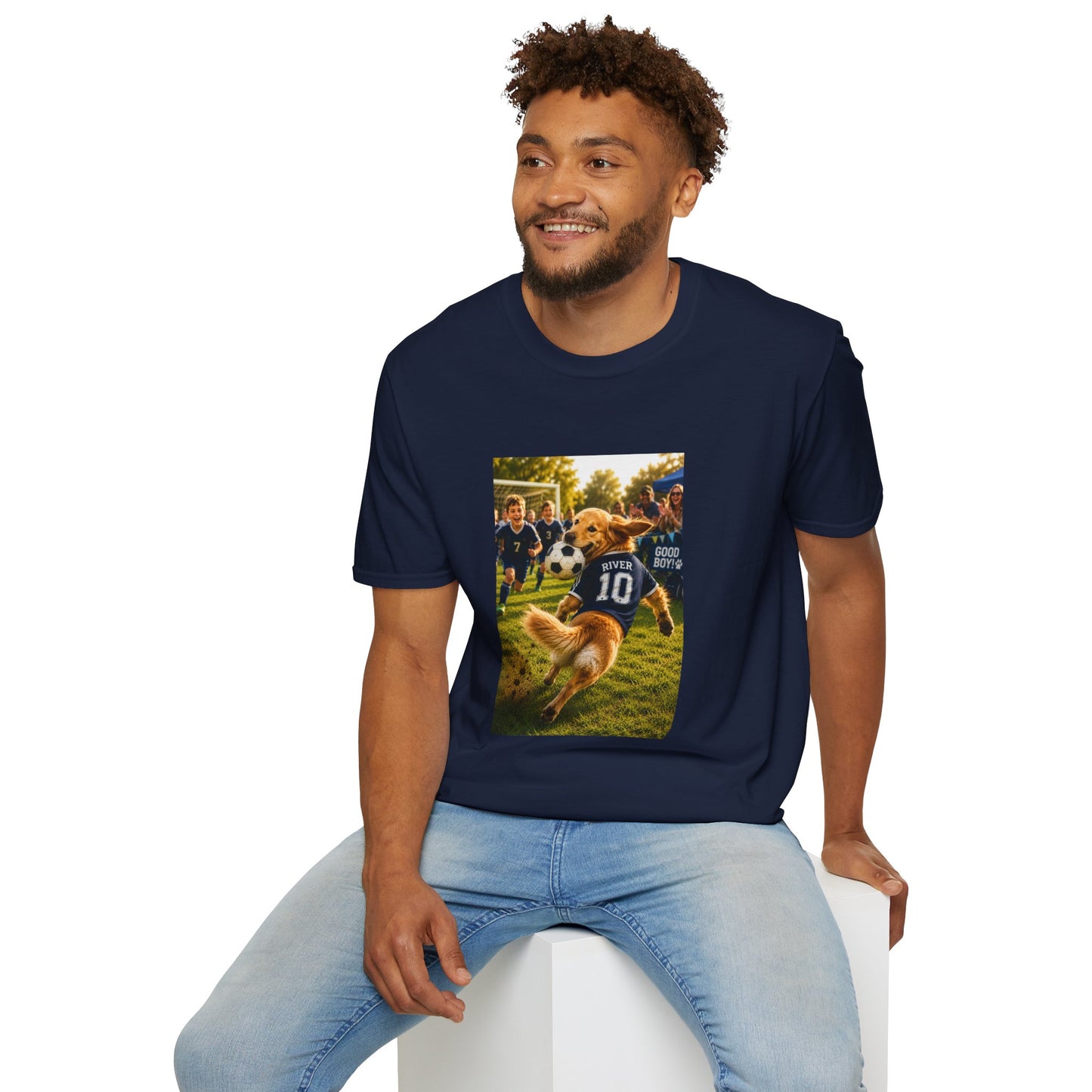 A man wearing a navy blue t-shirt with a custom graphic print of a dog playing fsoccer, paired with light blue jeans, sitting on a white block against a white background.