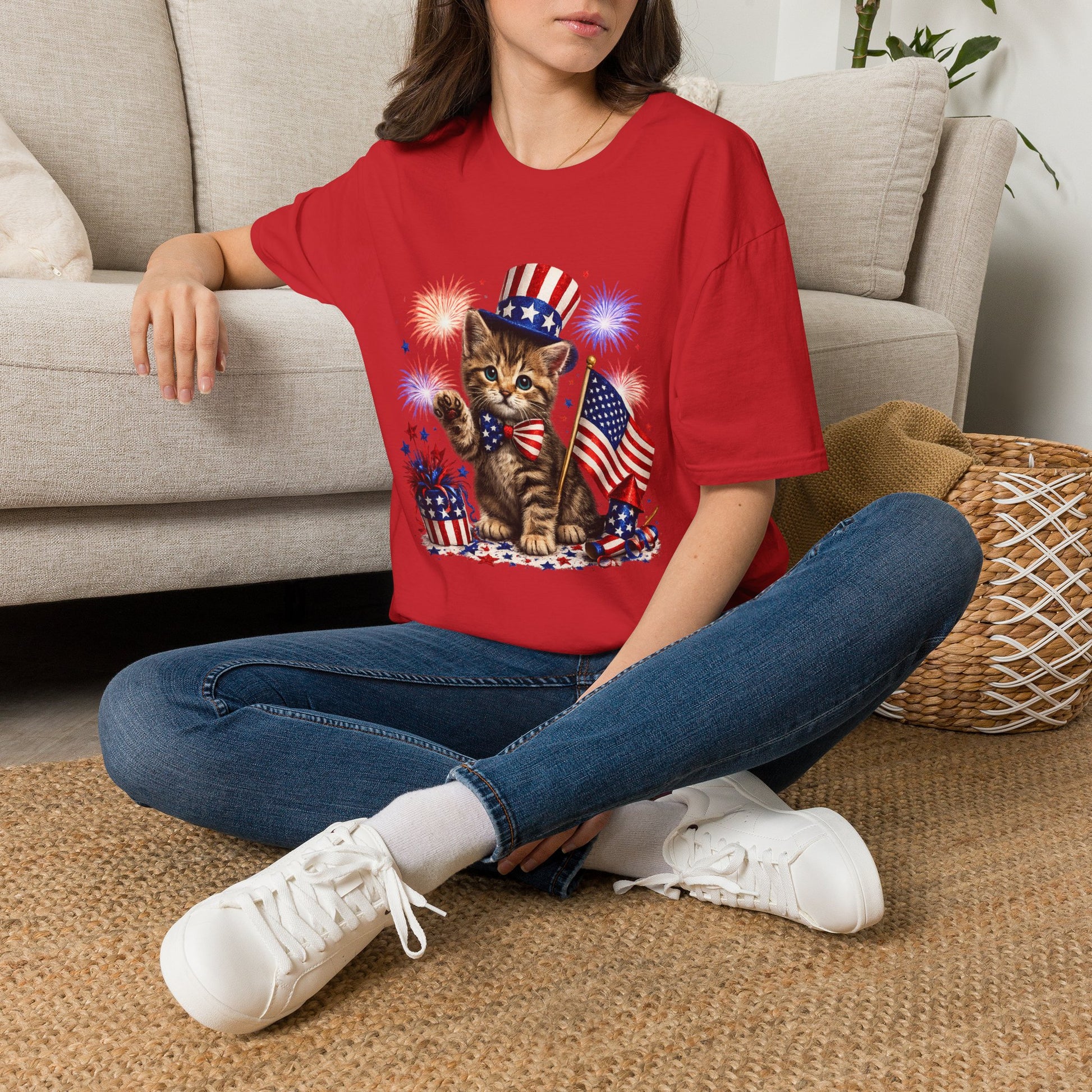 Person wearing a red t-shirt with a cat graphic sitting on a carpeted floor.