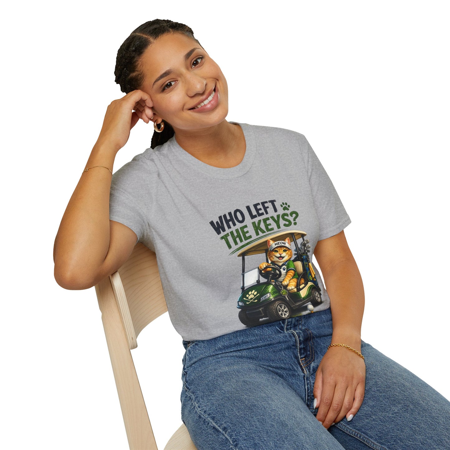 A woman sitting on a wooden chair wearing a heather gray graphic t-shirt with the text 'WHO LEFT THE KEYS?' and a cartoon cat in a golf cart, paired with blue jeans against a white background.