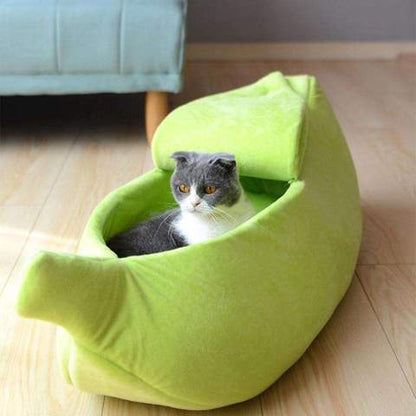 Cat lying in a green banana-shaped pet bed on a wooden floor.