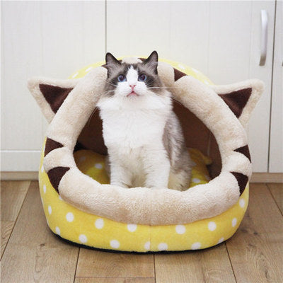 Cat sitting in a yellow pet bed with brown ears on a wooden floor.