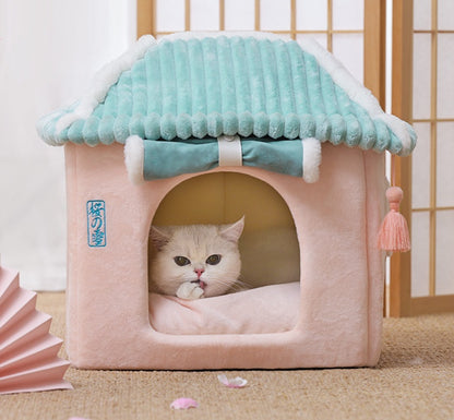 Cat lying inside a pink pet house with a teal roof on a wooden floor.