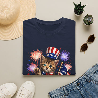 Navy blue t-shirt with a kitten wearing an American flag hat and fireworks design, surrounded by a hat, sunglasses, and jeans on a light background.