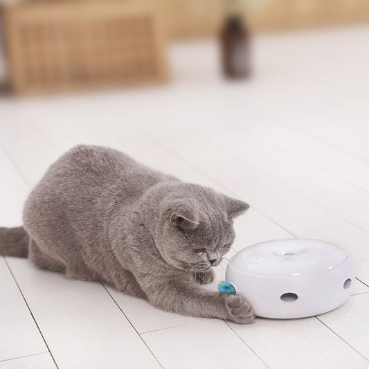 Cat playing with a white electronic device on a tiled floor.