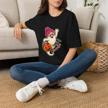 A woman sitting cross-legged on a woven rug in front of a beige sofa, wearing an black graphic T-shirt with a cartoon ghost holding a jack-o'-lantern and flowers, paired with blue jeans and white sneakers.