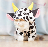 Small animal wearing a cow-themed costume with yellow horns and black and white pattern.