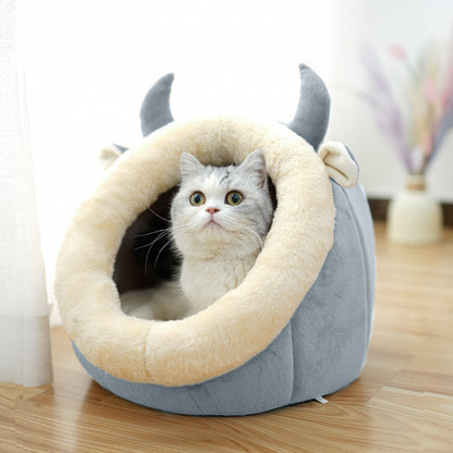 Cat peeking out from a gray pet bed with animal ears on a wooden floor.
