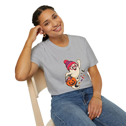A woman wearing a light gray crewneck t-shirt with a cartoon graphic of a ghost in a pink beanie holding a jack-o'-lantern, paired with blue jeans, seated on a wooden chair against a white background.