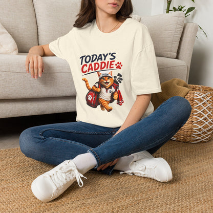 An natural short-sleeve crewneck t-shirt featuring a cartoon graphic of an orange tabby cat wearing a cap and holding golf clubs, with the text 'TODAY'S CADDIE' 