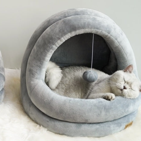 Cat lying inside a gray pet bed with a small hanging toy.