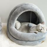 Cat lying inside a gray pet bed with a small hanging toy.