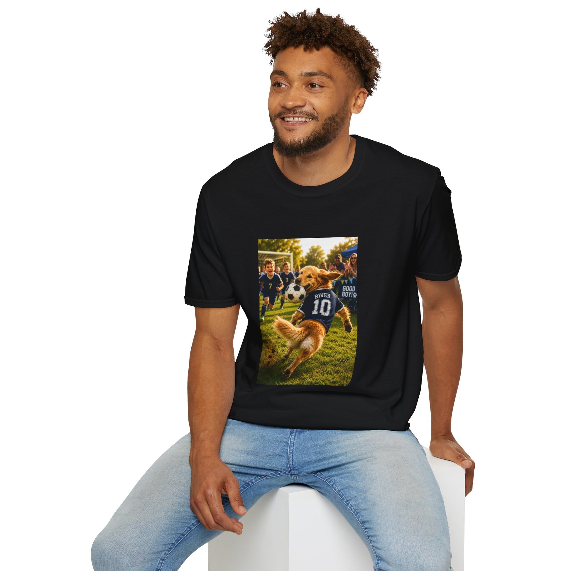 A man wearing a black graphic t-shirt and light blue jeans, sitting on a white block against a plain white background. The t-shirt features a rectangular graphic print showing a golden retriever dog playing football with players wearing navy jerseys.