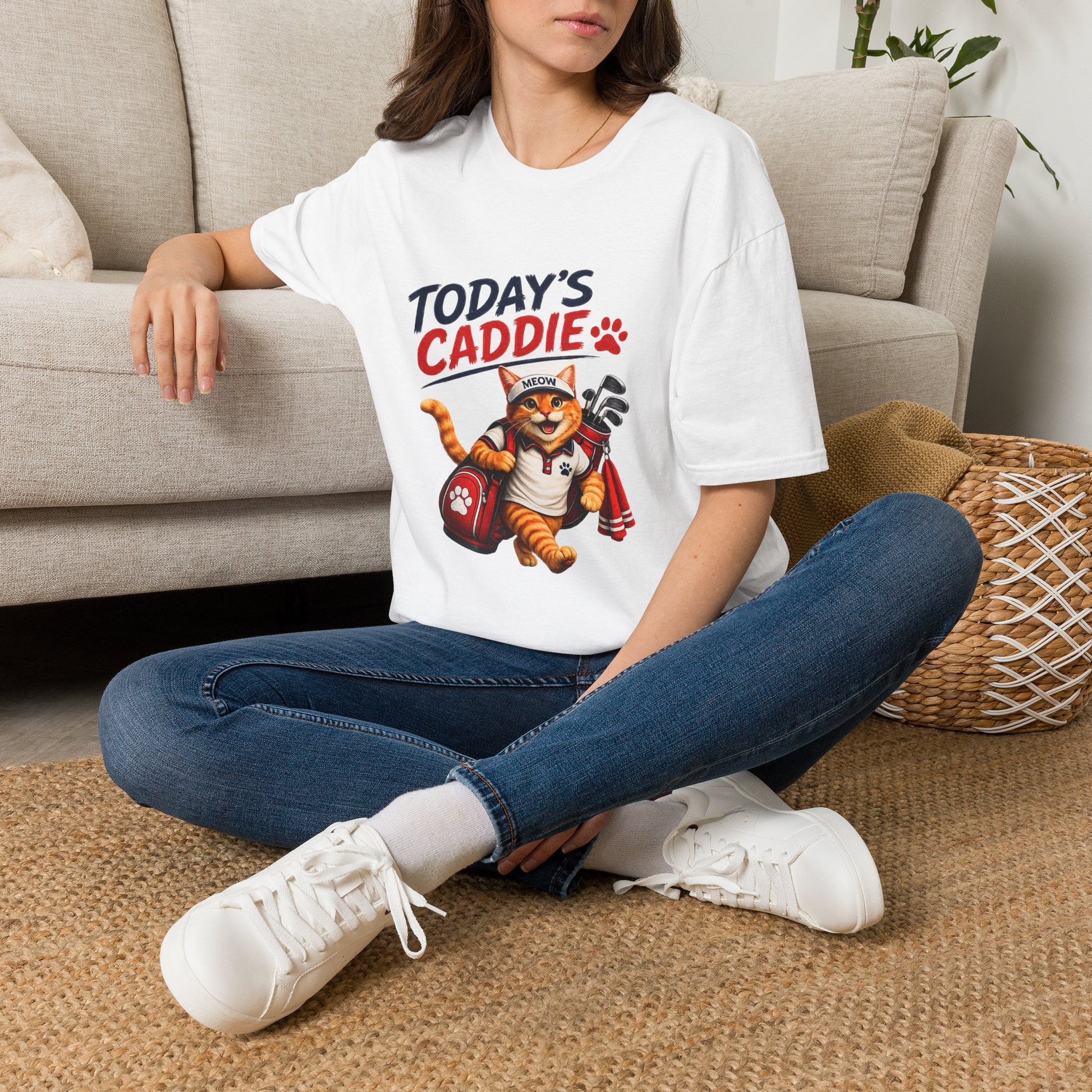 An white short-sleeve crewneck t-shirt featuring a cartoon graphic of an orange tabby cat wearing a cap and holding golf clubs, with the text 'TODAY'S CADDIE' 